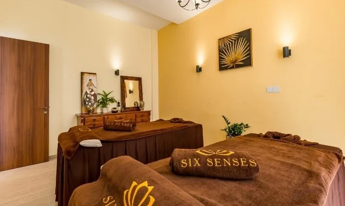 The Six Sense Spa treatment room — twin massage tables draped in embroidered brown blankets under warm yellow walls